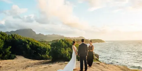 A bride and groom standing on a rocky coastal cliff facing an officiant during a wedding ceremony.