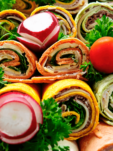 A close-up photograph of assorted food pinwheels garnished with radishes, tomatoes, and parsley.