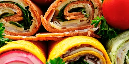 A close-up photograph of assorted food pinwheels garnished with radishes, tomatoes, and parsley.