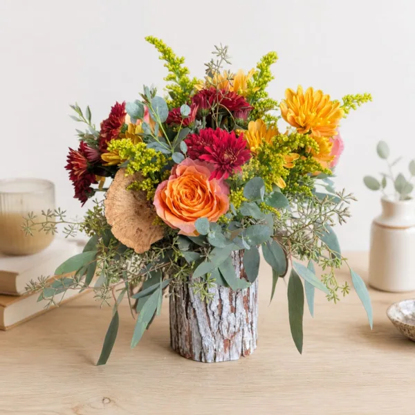 A mixed bouquet featuring orange roses, red dahlias, and greenery in a bark-covered vase.