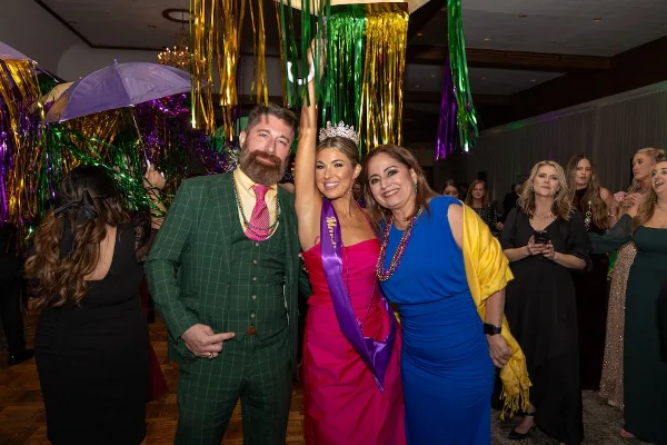 A professional photograph of a bride and groom at a festive event, surrounded by guests and colorful streamers.