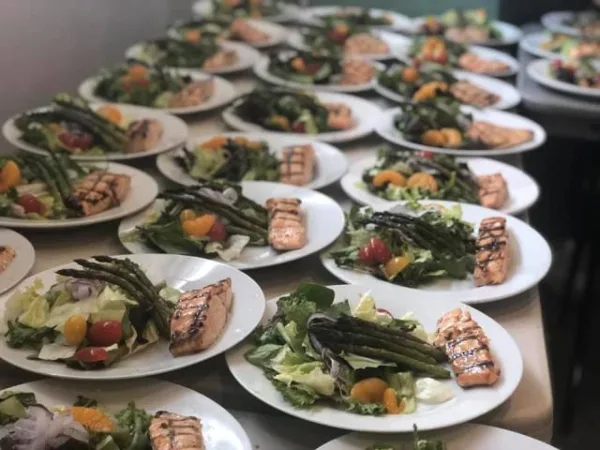 Rows of plated catering meals featuring grilled salmon and salad on a table.