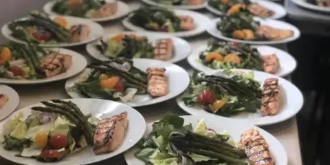 Rows of plated catering meals featuring grilled salmon and salad on a table.