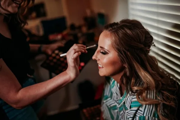 A makeup artist applying eye makeup to a smiling female client.