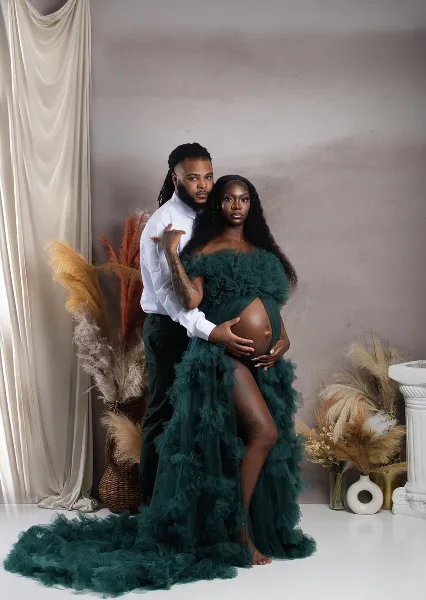 A professional studio photograph of a couple posing together, with the woman wearing a green ruffled dress and the man in a white shirt.