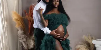 A professional studio photograph of a couple posing together, with the woman wearing a green ruffled dress and the man in a white shirt.