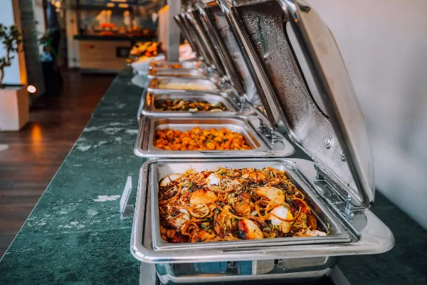 A catering buffet line with multiple stainless steel chafing dishes filled with prepared food.