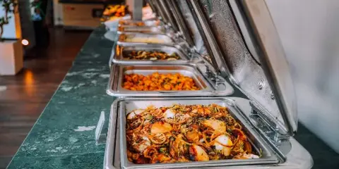 A catering buffet line with multiple stainless steel chafing dishes filled with prepared food.