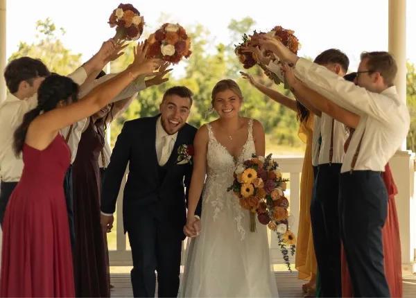 A bride and groom walking through a celebratory arch formed by their wedding party holding bouquets.