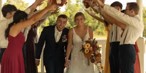 A bride and groom walking through a celebratory arch formed by their wedding party holding bouquets.