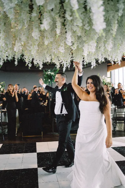 A bride and groom dancing under a large hanging floral installation in a wedding venue.