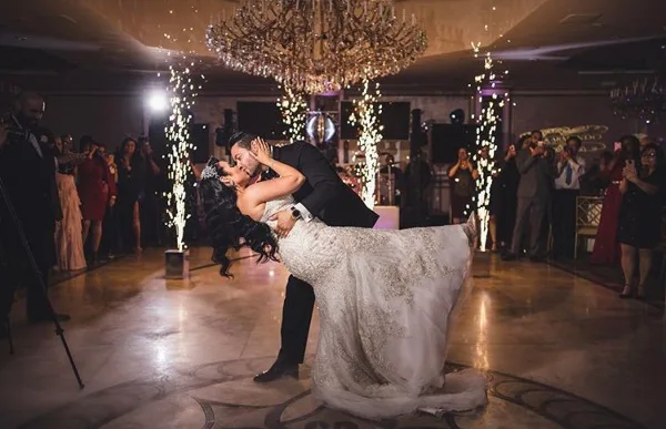 A bride and groom dancing at a wedding reception with sparkler effects and a DJ booth in the background.
