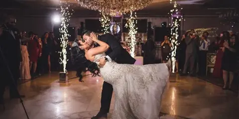 A bride and groom dancing at a wedding reception with sparkler effects and a DJ booth in the background.