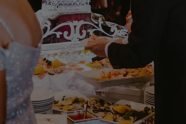 A catering staff member serving shrimp and oysters from a buffet station at an event.