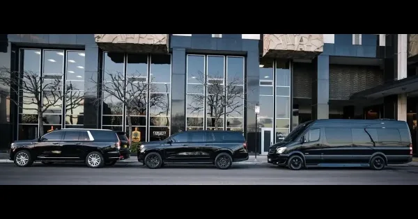 A lineup of black luxury SUVs and a passenger van parked in front of a modern glass building with the company name visible.