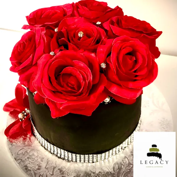 Black custom cake decorated with large red roses and jeweled accents.