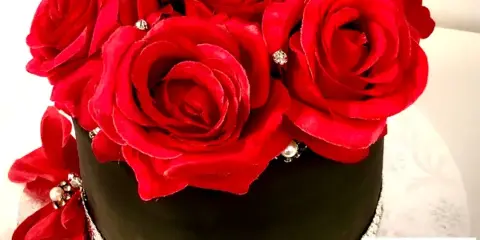 Black custom cake decorated with large red roses and jeweled accents.