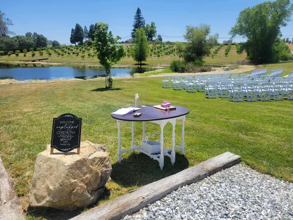 White folding chairs and a table set up on a grassy lawn near a pond for an event.