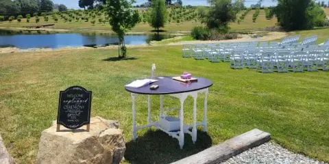 White folding chairs and a table set up on a grassy lawn near a pond for an event.