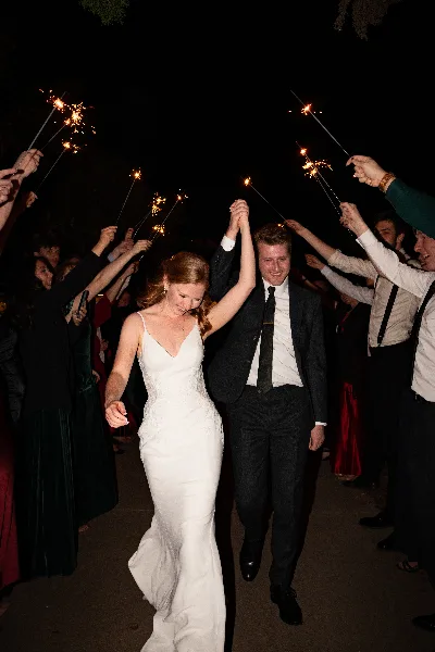 A bride and groom walking hand-in-hand through a crowd of guests holding lit sparklers at night.