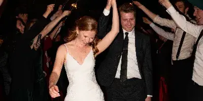 A bride and groom walking hand-in-hand through a crowd of guests holding lit sparklers at night.