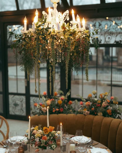 A wedding table setting featuring a large floral chandelier with candles and a matching floral centerpiece on a round table.