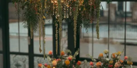 A wedding table setting featuring a large floral chandelier with candles and a matching floral centerpiece on a round table.