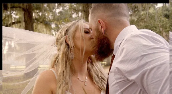A cinematic close-up of a bride and groom kissing outdoors, featuring the bride's veil and jewelry.