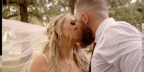 A cinematic close-up of a bride and groom kissing outdoors, featuring the bride's veil and jewelry.
