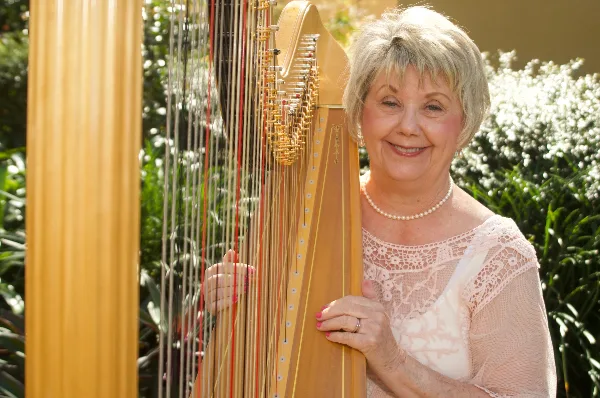 A smiling woman standing next to a large wooden concert harp outdoors.