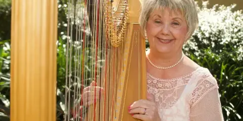 A smiling woman standing next to a large wooden concert harp outdoors.