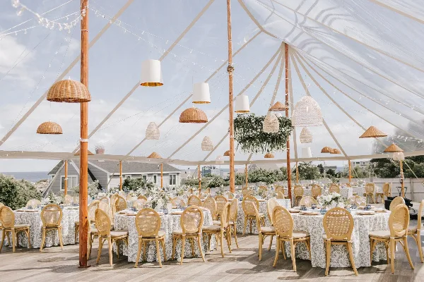 Interior of a clear geodesic wedding tent with round tables, white floral centerpieces, and hanging woven pendant lights.