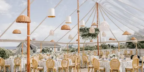 Interior of a clear geodesic wedding tent with round tables, white floral centerpieces, and hanging woven pendant lights.