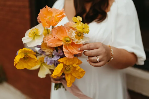 A bride in a white dress holding a colorful bouquet of orange, yellow, and white flowers.