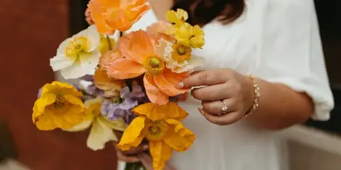 A bride in a white dress holding a colorful bouquet of orange, yellow, and white flowers.