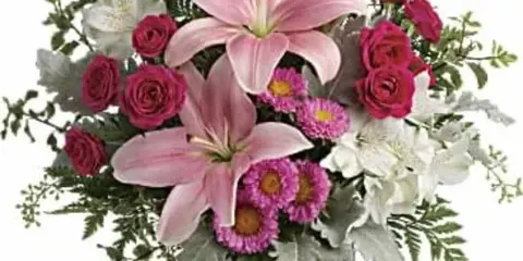 A floral arrangement with pink lilies, red roses, and white alstroemeria in a clear glass vase.