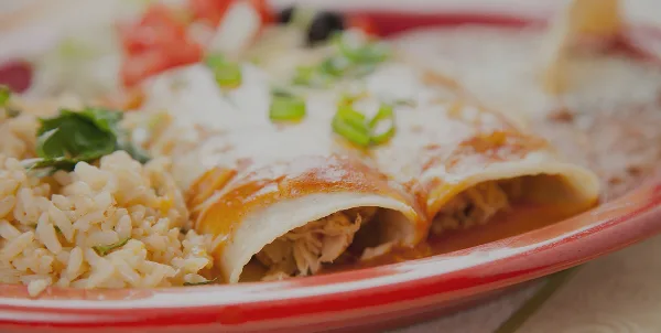 A plate of Mexican enchiladas topped with sauce and green onions, served with rice.
