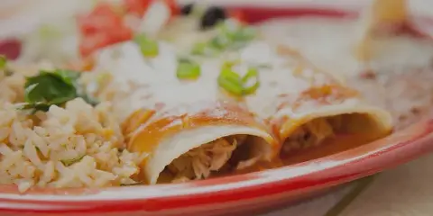 A plate of Mexican enchiladas topped with sauce and green onions, served with rice.
