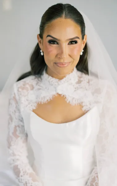 Portrait of a smiling bride wearing a white lace wedding dress and veil.
