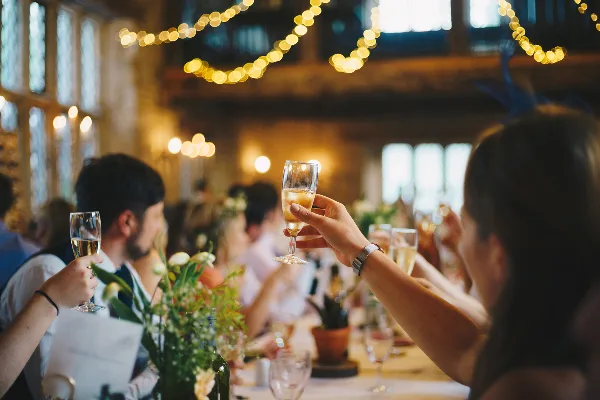 Guests at a banquet table raising champagne flutes in a toast under string lights.