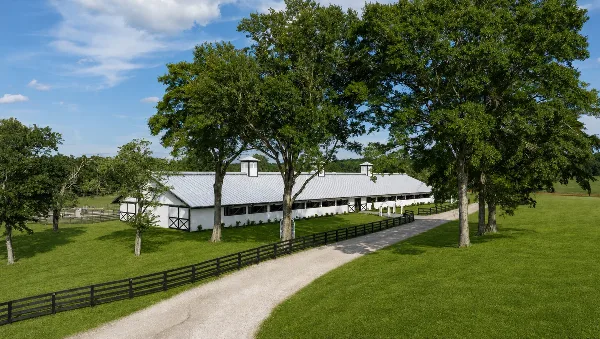 Exterior view of the Grand Pavilion at Dogwood Reserve, a white barn-style structure with a metal roof and cupolas, situated on a green lawn with a gravel driveway and black fencing.