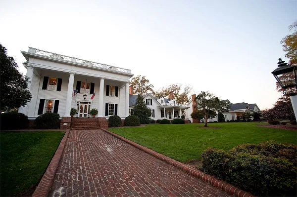 Exterior view of a white historic manor house with a brick walkway and manicured lawn.
