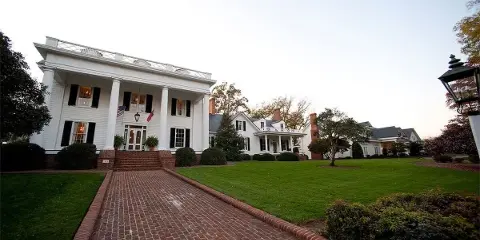 Exterior view of a white historic manor house with a brick walkway and manicured lawn.