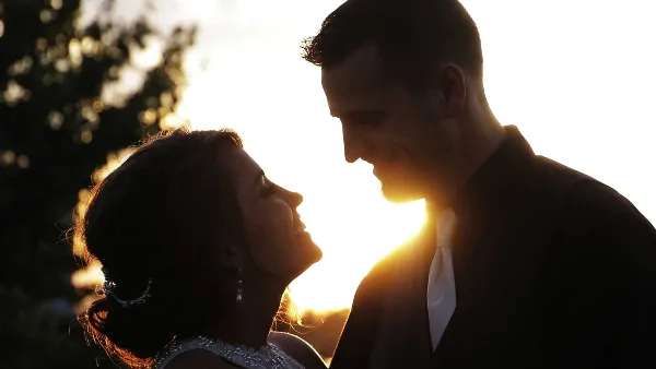 A cinematic, backlit silhouette of a bride and groom looking at each other during a wedding.