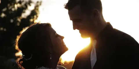 A cinematic, backlit silhouette of a bride and groom looking at each other during a wedding.