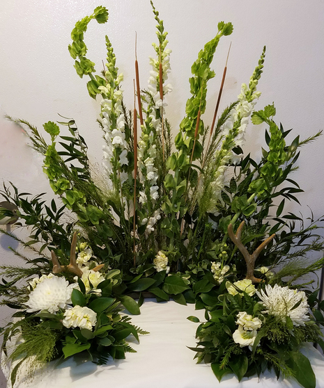 A custom floral arrangement with white flowers, greenery, and antlers on a white surface.