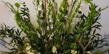 A custom floral arrangement with white flowers, greenery, and antlers on a white surface.
