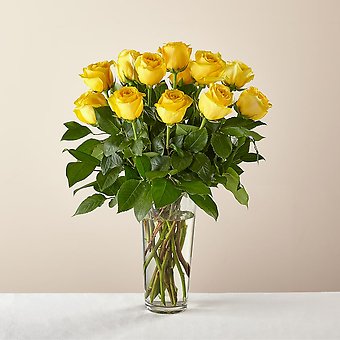 A bouquet of long-stem yellow roses arranged in a clear glass vase.