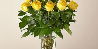 A bouquet of long-stem yellow roses arranged in a clear glass vase.