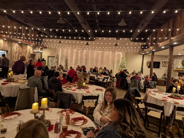 Interior view of the event center with round tables, string lights, and guests seated.